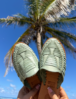 Pair of sandals held up with a palm tree and blue sky in the background